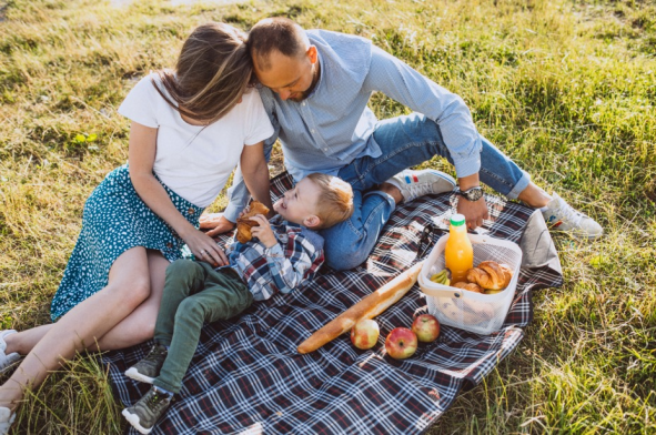 a man, a woman, a young boy laugh on a blanket while picnicking at Millican Reserve